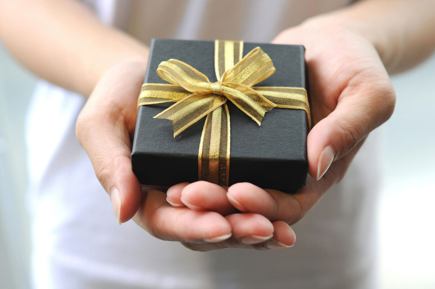 Betekenisvolle cadeau in luxe zwarte cadeauverpakking met gouden strik in handen vastgehouden