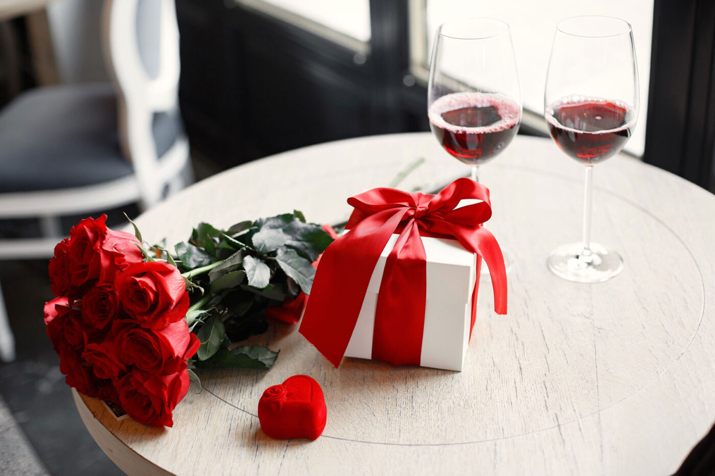 Origineel Valentijnscadeau met rode rozen, ingepakt cadeau en glazen wijn als symbool voor kleine romantische gebaren