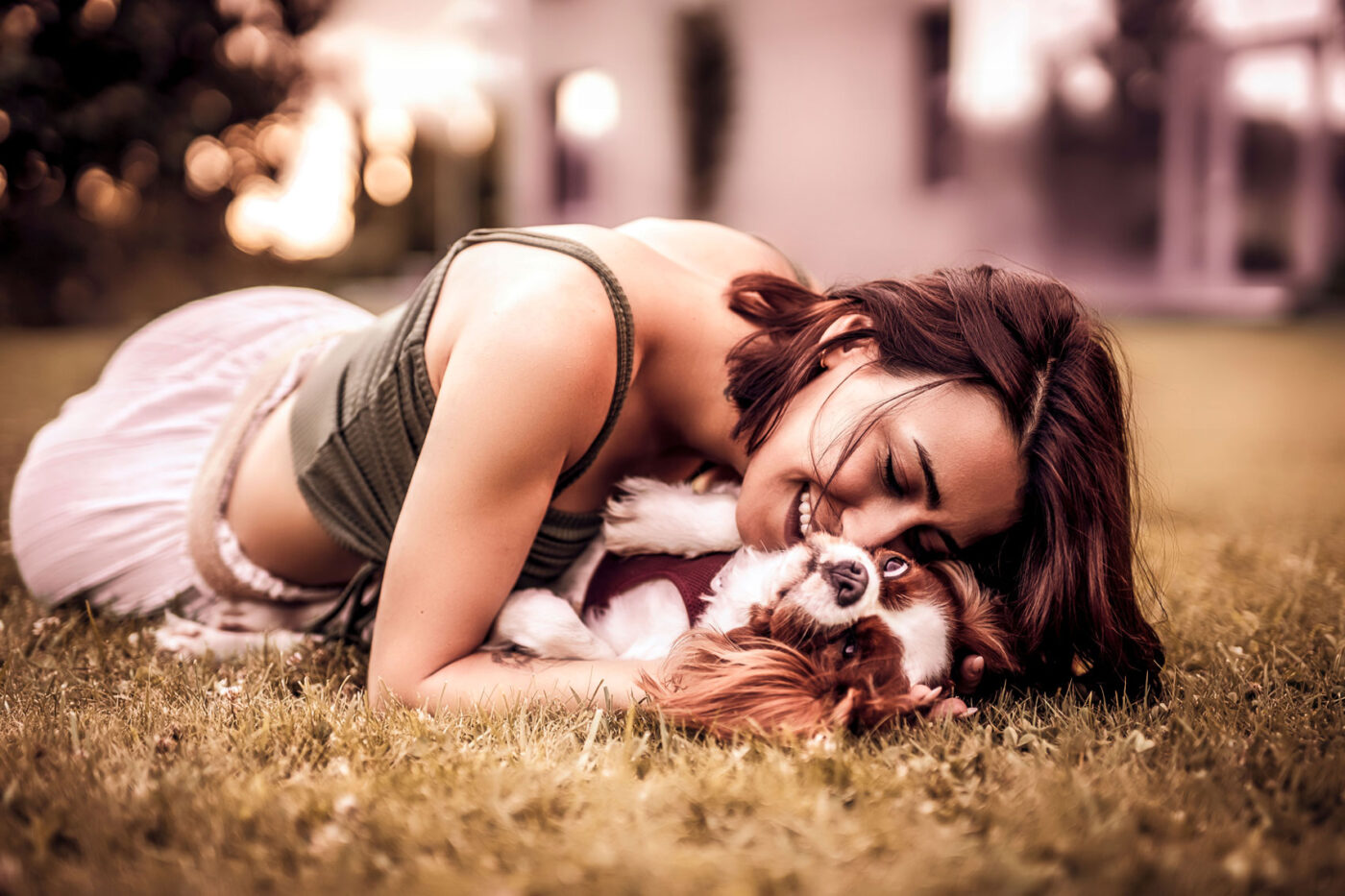 Vrouw ligt in het gras en knuffelt een bruin-witte hond.