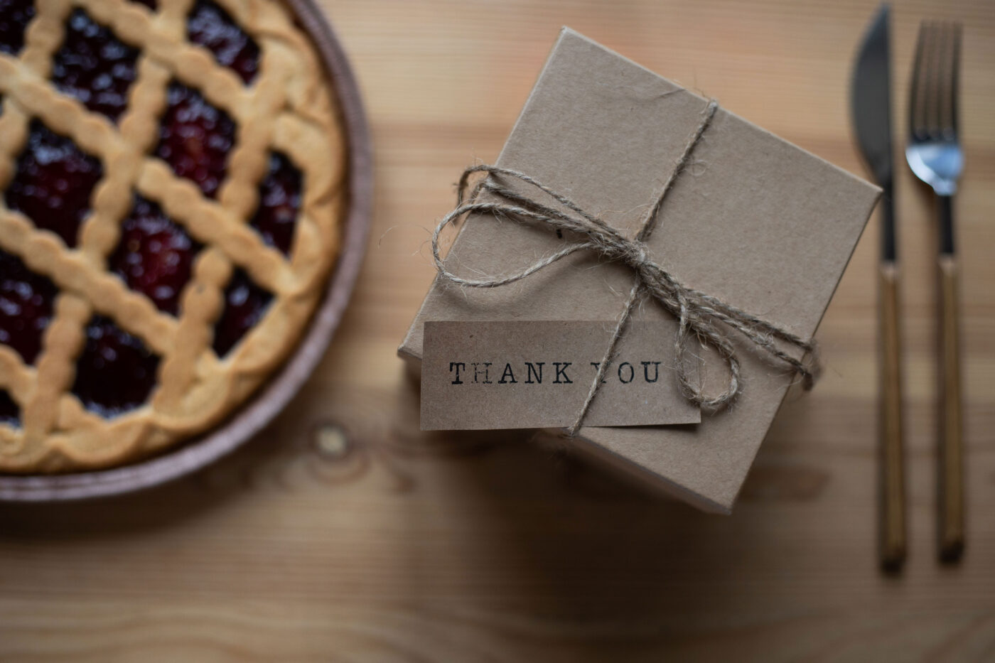 Bruin cadeaudoosje met touw en een kaartje met ‘Thank you’, naast een taart op een houten tafel.